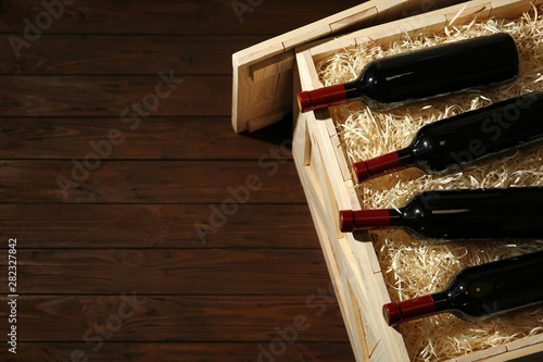 Crate with bottles of wine on wooden background. Space for text