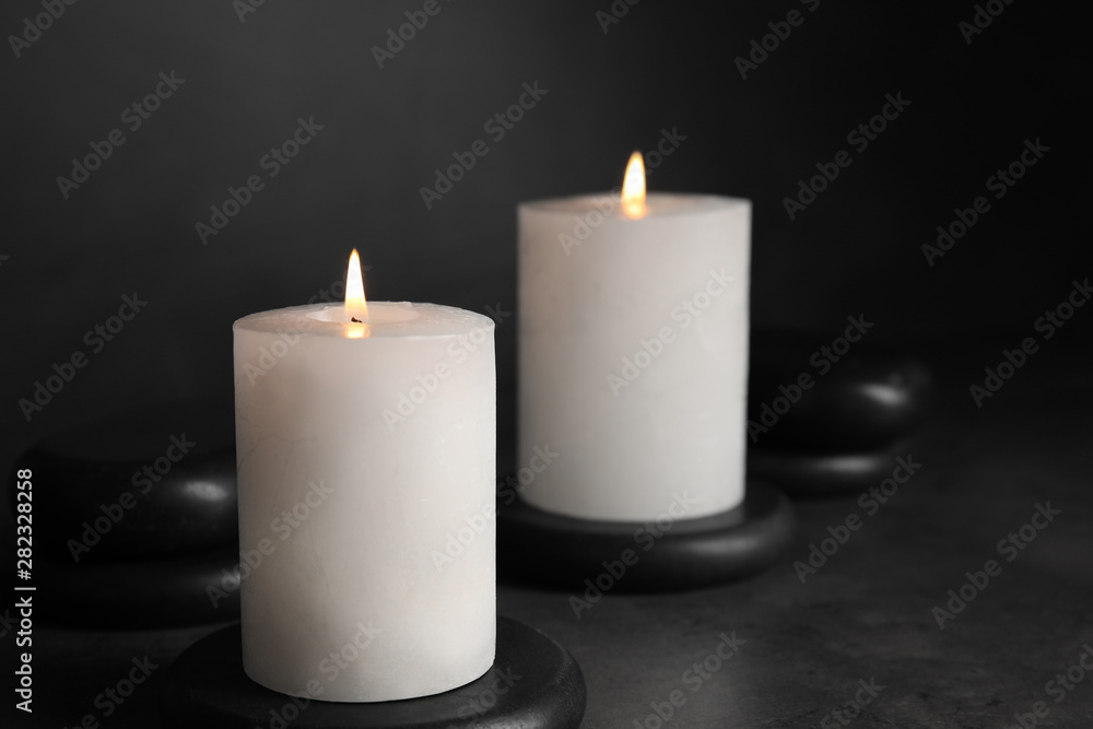 Burning candles and black spa stones on grey table Burning candles and black spa stones on grey table