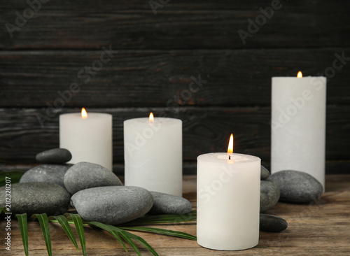 Burning candles, spa stones and palm leaf on wooden table