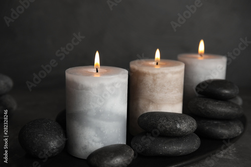 Burning candles and spa stones on black plate, closeup