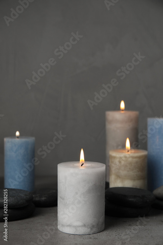 Burning candles and spa stones on grey table, space for text