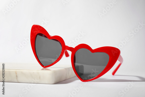 Stylish heart shaped sunglasses on board against white background