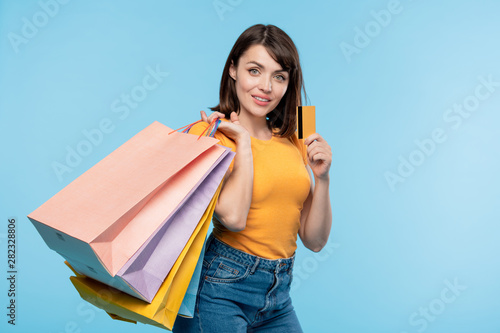 Photos Happy young shopaholic with several paperbags boasting with credit card
