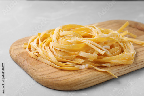 Board with uncooked egg noodles on grey table, closeup