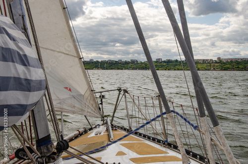 The bow of a sailing boat amid waves and an approaching shore.