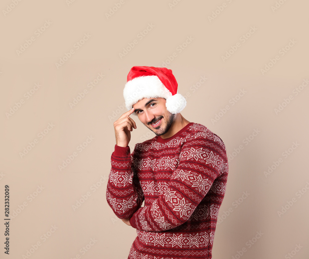 Portrait of young man in Christmas sweater and Santa hat on beige background Portrait of young man in Christmas sweater and Santa hat on beige background