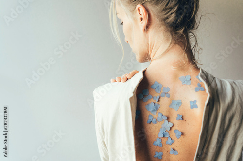 The dress is spread out on the back of a beautiful Caucasian blond woman, on a naked body are flower petals, many freckles and moles on the skin. Natural beauty