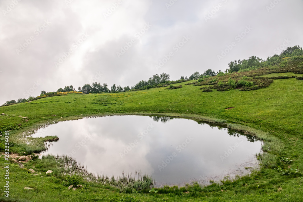 View of a mountain lake with clear water and reflection at cloudy summer day. View of a mountain lake with clear water and reflection at cloudy summer day.
