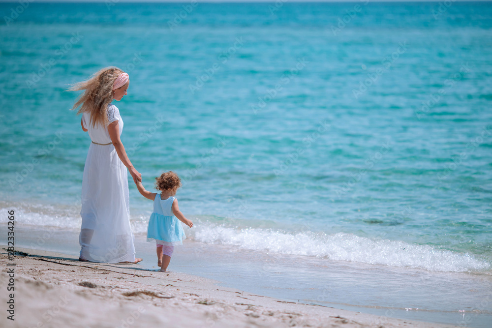 Mom in a white dress and a little daughter in a turquoise dress on the beach.