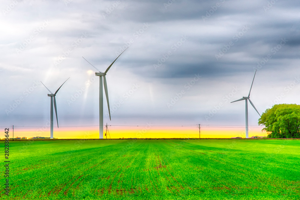 Wind power plant turbines on a green field under sky with clouds on sunset. Green energy, renewable sources, save planet Wind power plant turbines on a green field under sky with clouds on sunset. Green energy, renewable sources, save planet
