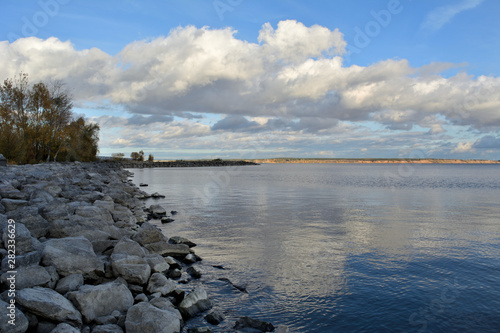 Picturesque landscape with river, trees on rocky bank and clouds in the sky. © Happy Dragon