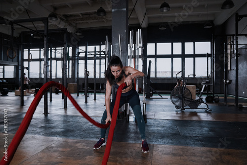 Fit woman using battle ropes during strength training at the gym.