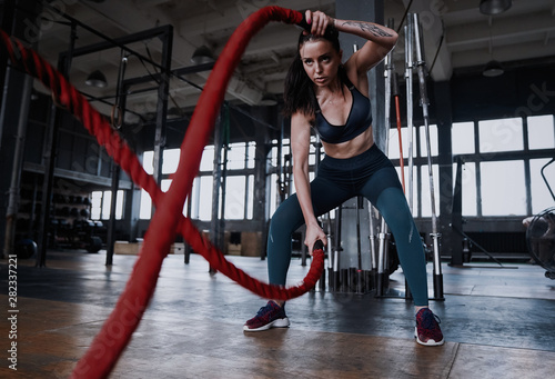 Fit woman using battle ropes during strength training at the gym. © opolja
