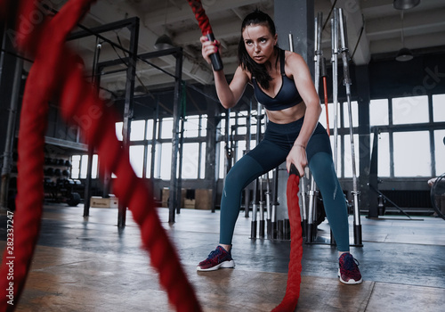 Fit woman using battle ropes during strength training at the gym.