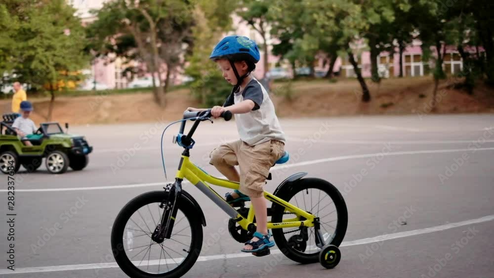 Child riding bicycle in park at sunset light. Kid in helmet learning to ride at summer. Happy boy riding bike, having fun outdoors on nature. Active sport family leisure. Healthy holidays. Slow motion Child riding bicycle in park at sunset light. Kid in helmet learning to ride at summer. Happy boy riding bike, having fun outdoors on nature. Active sport family leisure. Healthy holidays. Slow motion