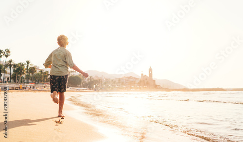 Happy little boy running by Mediterranean spain coast in Sitges town near Barcelona photo