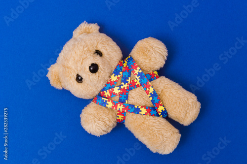 World Autism Awareness day, mental health care concept with teddy bear and ribbon puzzle pattern. On blue background.