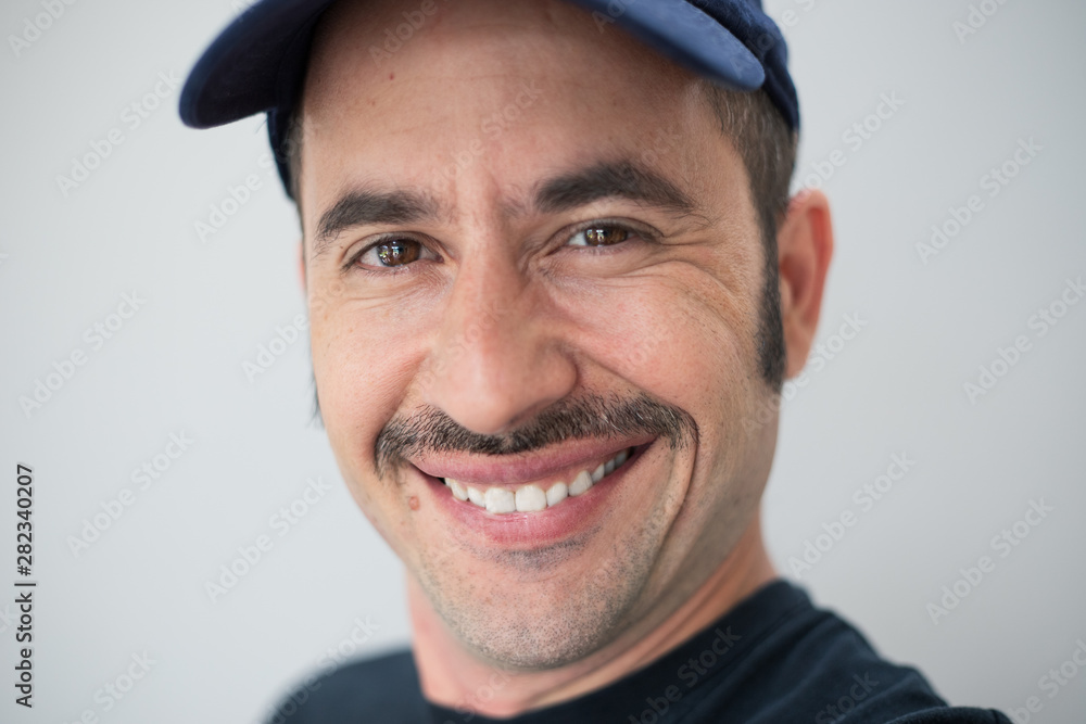 White male with a prominent mustache and a hat against a seamless background looks at the camera and smiles White male with a prominent mustache and a hat against a seamless background looks at the camera and smiles