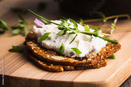 A delicious garlic and chive cream cheese spread on herbed crackers stacked on a bamboo cutting board.
