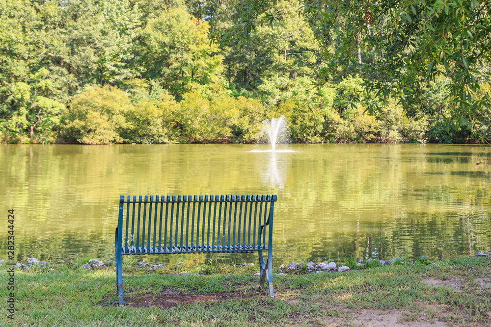Obraz premium Neighborhood Fountain, Pond or Lake, and Bench: Neighborhood water fountain, pond or lake, and sitting bench with thick green forest backdrop. Peace and serenity concept.