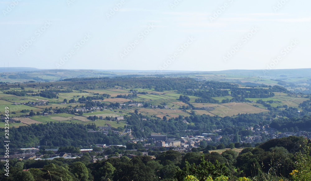a panoramic view of the countryside around sowerby bridge in west yorkshire with buildings of the town surrounded by farms and fields in a pennine landscape
