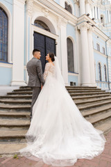 Wedding couple. Beautiful bride in a luxurious white wedding dress and elegant groom look at each other near the church. Stylish newlywed couple. Marriage concept