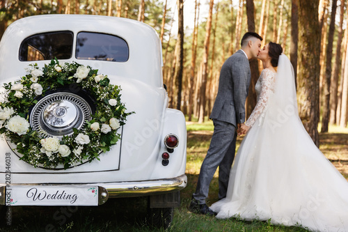 Wedding couple kissing near Wedding car with bouquet and the word 