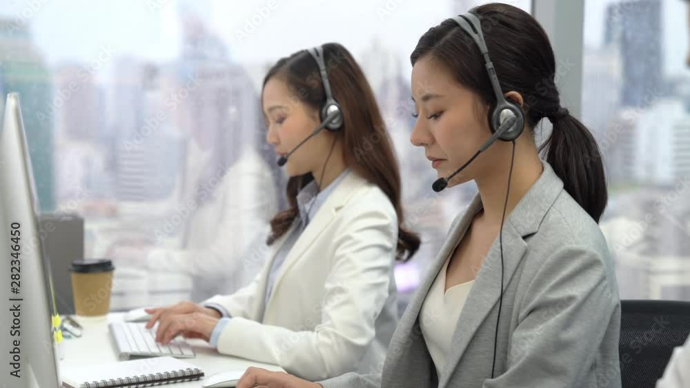 Beautiful woman Asian customer service operators talking on headsets and using computer at call center office with team Beautiful woman Asian customer service operators talking on headsets and using computer at call center office with team