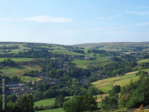 a panoramic view of the village of luddenden in west yorkshire surrounded by fields mills and trees in summer sunlight