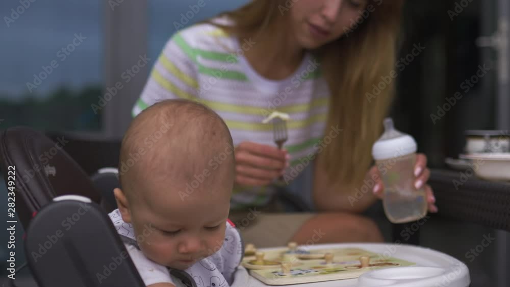 Young mother feeding her baby boy son sitting in a child seat - Family values warm color summer scene Young mother feeding her baby boy son sitting in a child seat - Family values warm color summer scene