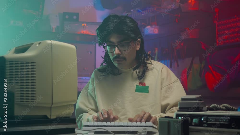 In the '80s or '90s young man using his personal computer typing on a keyboard. Retro scene with vintage colors and atmosphere.