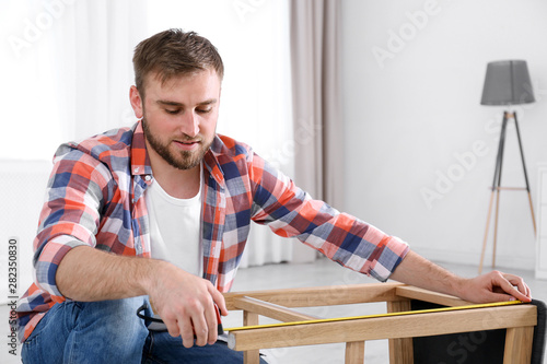 Young working man using measure tape at home