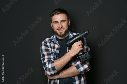 Young working man with power drill on dark background