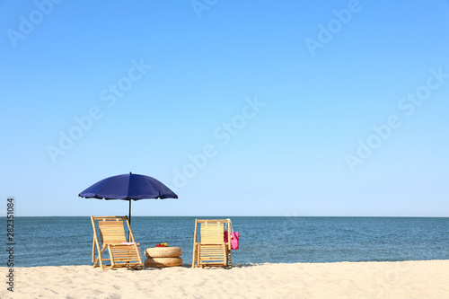 Empty wooden sunbeds and beach accessories on sandy shore