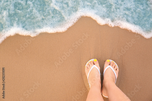 Top view of woman with white flip flops on sand near sea  space for text. Beach accessories