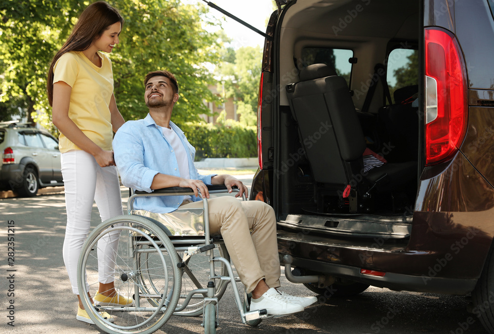 Young woman helping man in wheelchair to get into van outdoors Stock 写真
