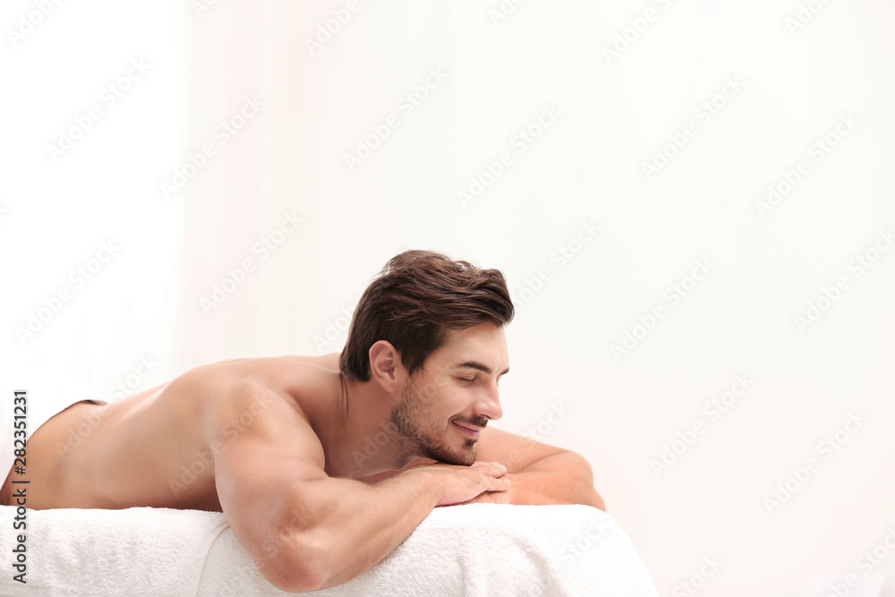 Handsome young man relaxing on massage table against light background, space for text. Spa salon Handsome young man relaxing on massage table against light background, space for text. Spa salon