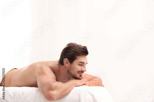 Handsome young man relaxing on massage table against light background  space for text. Spa salon