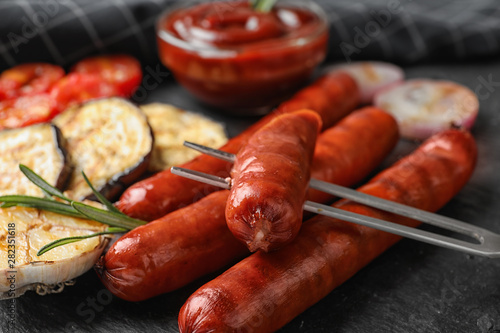 Delicious grilled sausages and vegetables on black table, closeup. Barbecue food