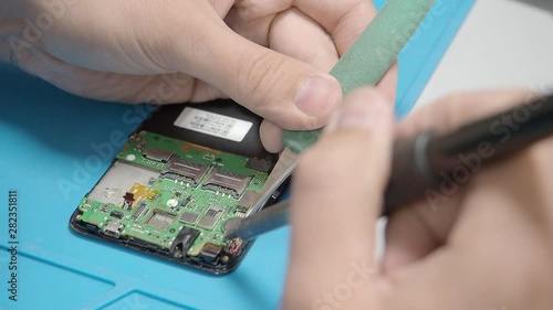 Smartphone assembling in repair shop. Soldering contact on circuit board with the soldering iron. Mobile phone maintenance service