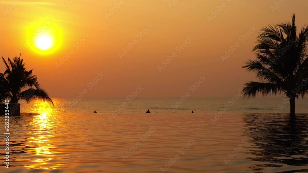 Gorgeous sunset with glowing sky reflected on the calm smooth surface of an infinity swimming pool overlooking a tropical beach. Peaceful romantic island paradise evening scene. Gorgeous sunset with glowing sky reflected on the calm smooth surface of an infinity swimming pool overlooking a tropical beach. Peaceful romantic island paradise evening scene.