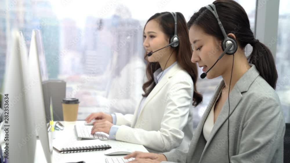 Asian customer service operator team talking on headsets and using computer at the call center office in the city Asian customer service operator team talking on headsets and using computer at the call center office in the city