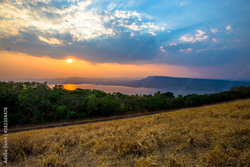 Obraz premium Natural panoramic wallpaper of high mountain scenery, overlooking the atmosphere of rivers, grasslands, roads, and the orange sunshine in the evening, blown through blurred cool air.