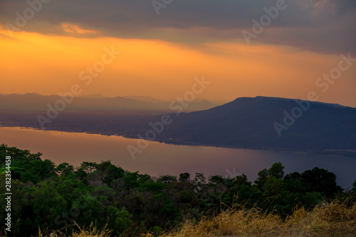 Natural panoramic wallpaper of high mountain scenery, overlooking the atmosphere of rivers, grasslands, roads, and the orange sunshine in the evening, blown through blurred cool air. © bangprik