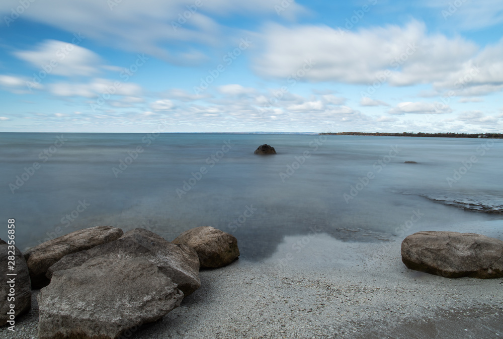 Rocks on sandy beach and calm water with blue sky and clouds