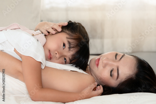 asian mother laying on bed and holding little girl daughter together with love