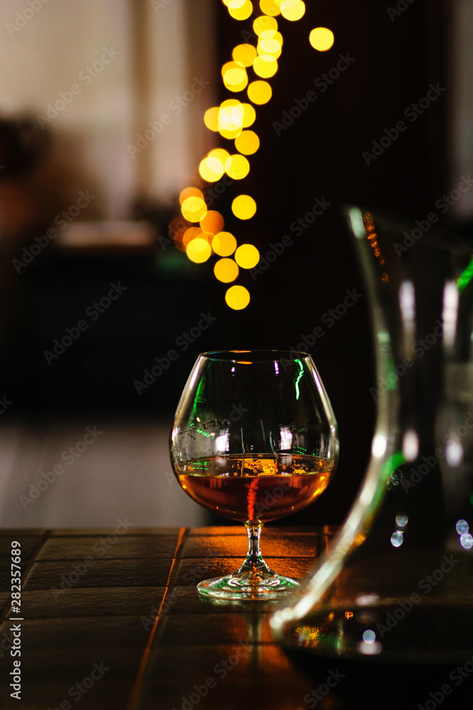 Snifter of brandy in elegant glass with space for text on dark colorful background. Decanter defocussed. Traditional French drink. Stiff drink. Service and tasting concept.