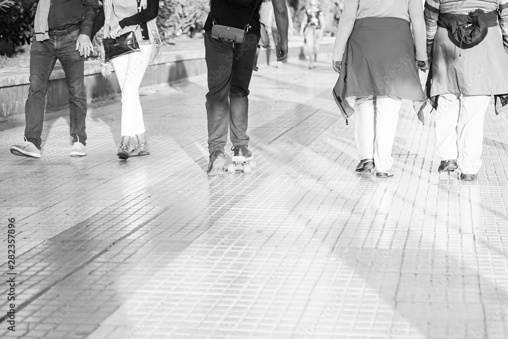 Obraz premium People walking down the street in the afternoon, beautiful sunlight . People walking and boy with skatebord listening to music. background black and white - Image