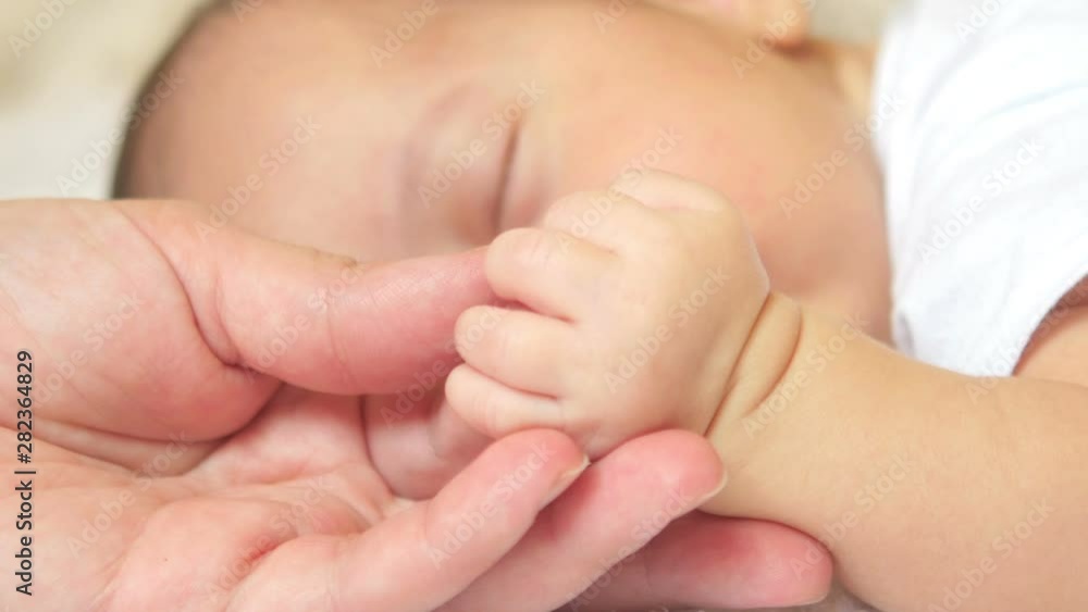 Motherhood. Mom’s hands gently stroke the fingers of a newborn baby. Motherhood. Mom’s hands gently stroke the fingers of a newborn baby.