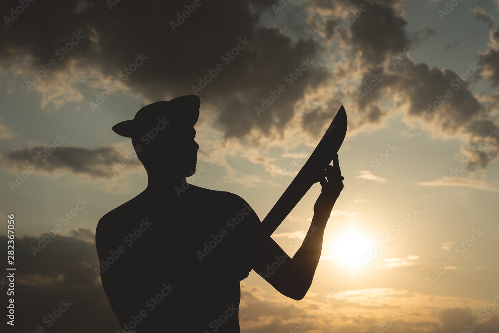 Silhouette of pirate man in a pirate hat and with a sword in hands over a evening cloudy sky background in sunset rays.